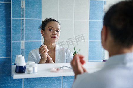 浴室镜子里的倒影是一位平静的女人，她用润肤霜按摩双手，呵护双手皮肤