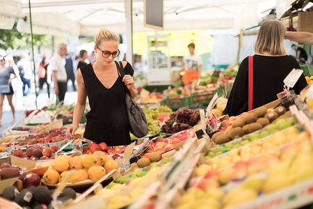 买水果摄影照片_在当地食品市场购买水果和蔬菜的妇女。