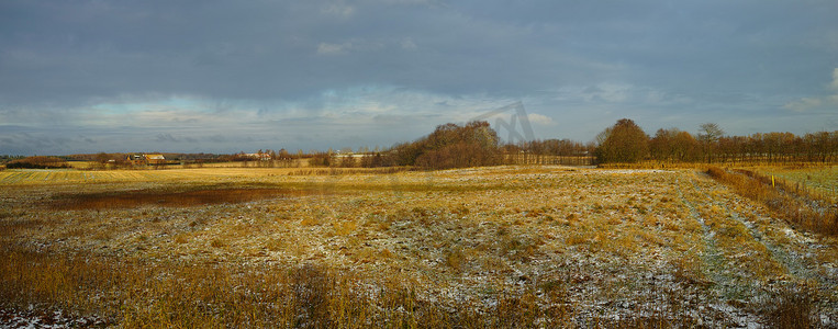 冬日田野的风景，草地上有一点雪，天空多云。