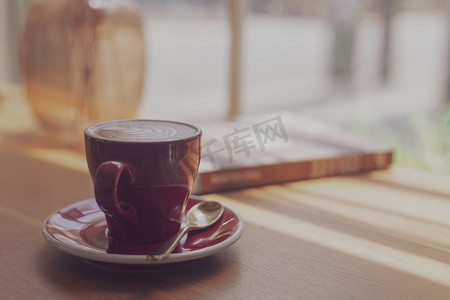 关闭热艺术拿铁咖啡，卡布奇诺咖啡在咖啡店木桌上的红杯中模糊背景与散景图像处理与复古风格