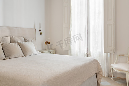 米色摄影照片_明亮的卧室内饰，舒适的床铺有米色床单，床头柜上放着干花。