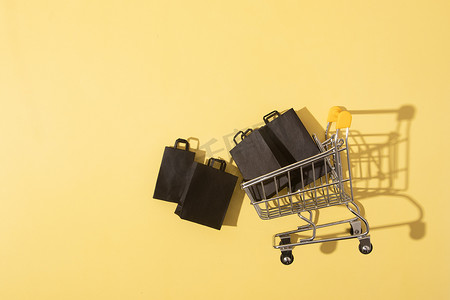 创意式摄影照片_黄色背景黑色星期五销售中带购物袋的平躺式微型超市推车