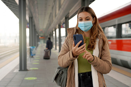 在火车站戴外科口罩的女旅客在户外用手机在线购票