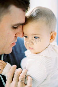 爸爸用鼻子摸着宝宝的额头，用手指握住宝宝的手。