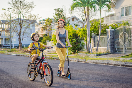 妈妈背包摄影照片_活跃的小学生男孩和他的妈妈戴着安全帽，在阳光明媚的日子里骑着背包骑自行车。