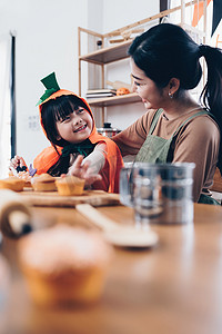 万圣节的年轻女孩和母亲在桌上做点心和纸杯蛋糕。