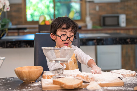 分割线可爱摄影照片_可爱的亚洲小男孩在家庭厨房里用筛子筛漏勺筛面团面粉，准备烘焙面包店和蛋糕。