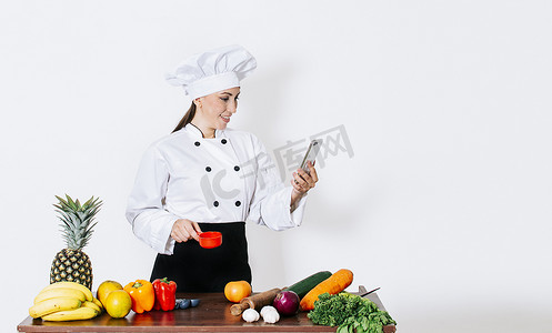 女厨师桌上摆着蔬菜，用智能手机寻找食谱。