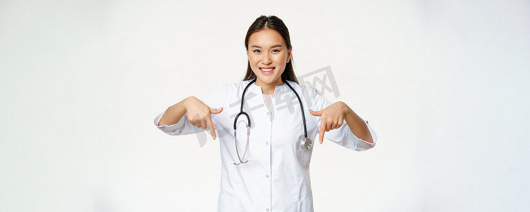 微笑的亚洲女医生，手指向下，展示促销优惠、诊所服务折扣、医院广告、白色背景