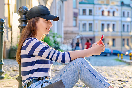 都市风格，坐在人行道上使用智能手机的时尚少女