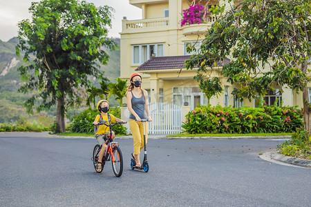 活跃的小学生男孩和他的妈妈戴着医用面罩和安全头盔，在阳光明媚的日子里骑着背包骑自行车。
