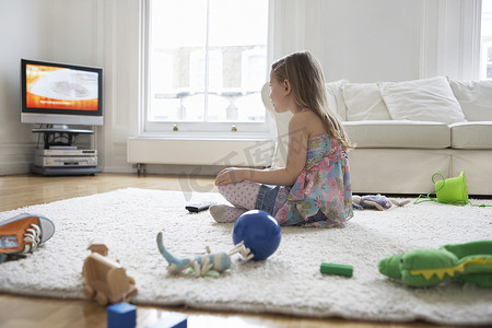一个小女孩在地板上玩玩具看电视的侧视图