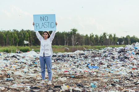保护环境海报摄影照片_女志愿者在垃圾填埋场举着无塑料海报，积极分子与环境污染作斗争