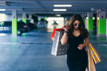 年轻美丽的快乐女人带着购物袋走进商场的地下通道到她的车里