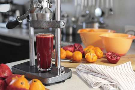 一杯鲜榨石榴汁、切碎的石榴、橘子和家里的石榴榨汁机
