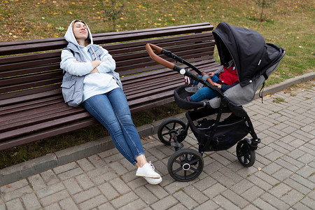 一名年轻女子带着孩子散步时睡在婴儿车旁边的长凳上