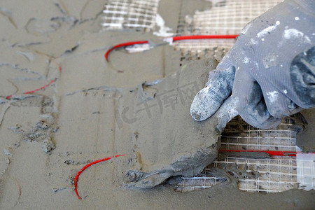 工人用抹刀在地暖电缆上涂抹水泥砂浆