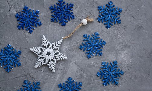 圣诞树上的一朵白色装饰以雪花和许多蓝色雪花的形式躺在灰色的混凝土背景上。