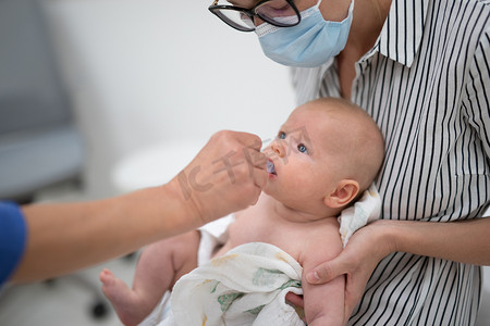 口服摄影照片_儿科医生在小婴儿母亲在场的情况下，为其口服轮状病毒感染疫苗。
