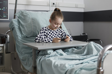 正在接受治疗的生病女孩在病床上休息，同时在智能手机上观看动画片