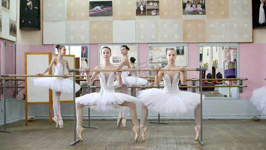在芭蕾舞厅，穿着白色芭蕾舞短裙的女孩们，包在芭蕾舞中，向前排练，年轻的芭蕾舞女演员穿着足尖鞋蹲在芭蕾舞厅的栏杆上。