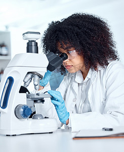 一位美丽的非洲裔美国年轻女性，留着爆炸头，穿着实验服，在实验室的显微镜下观察医学样本。