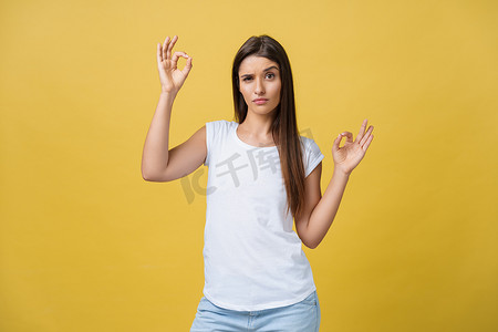 快乐的年轻女人用手指表现出好的手势，在黄色背景中眨眼