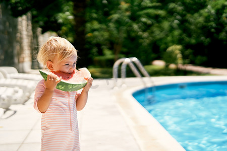 小女孩站在泳池边吃一块西瓜