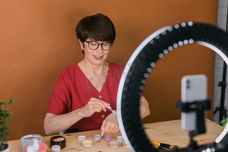 时影摄影照片_中年妇女在录制视频时用眼影、腮红调色板和刷子谈论化妆品。
