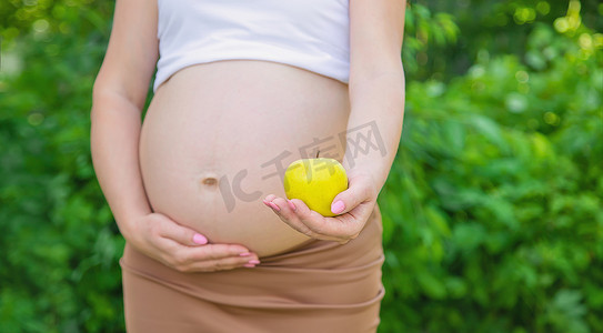 孕妇饮食摄影照片_孕妇手里拿着一个苹果。