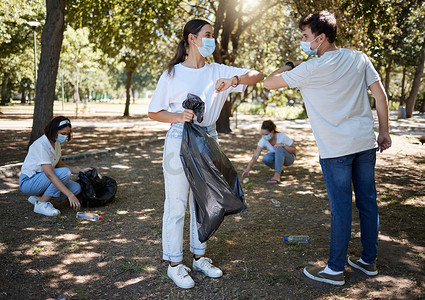 新冠疫情期间，清洁工和志愿者在打扫社区公园时戴着口罩，并用肘部手势表示感谢。