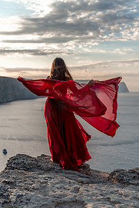 飘动摄影照片_一位身穿红裙的女子站在暴风雨的天空之上，她的裙子在风中飘扬，布料在风中飞舞。