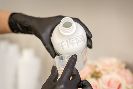 一位戴着黑手套的美发师正在美发沙龙里用瓶子准备染发剂，特写。
