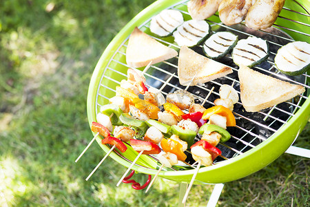 在野餐或夏季露营旅行期间，便携式烧烤站在绿色草坪上，有复制空间