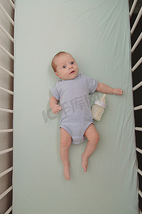 宝宝母乳摄影照片_婴儿床顶视图中拿着瓶子的婴儿。