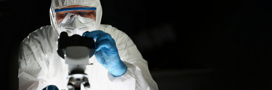 蓝色防护手套中的集中化学家在化学实验室看显微镜
