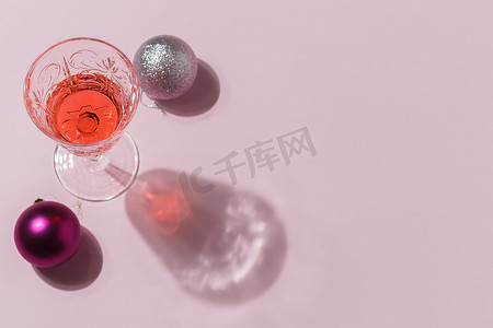 简约背景装饰图案摄影照片_粉红色背景的圣诞玩具的简约组合，玻璃杯里有鸡尾酒。