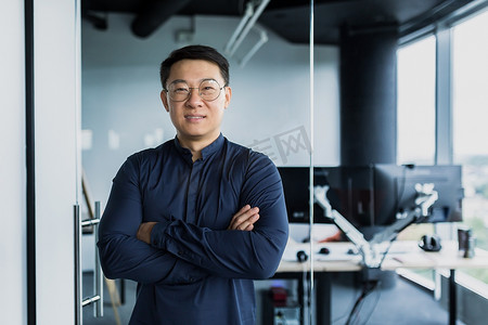 成功的亚洲程序员、团队领导公司老板微笑着交叉双臂看着镜头、在 IT 办公室内工作的才华横溢的创业企业家的肖像。