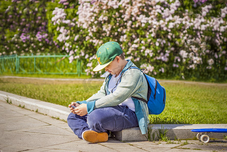 一个年轻人坐在淡紫色小巷的一侧，看着他的手机。