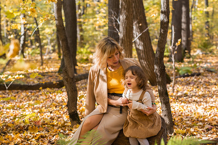 哭泣摄影照片_妈妈在秋天的大自然中安慰哭泣的小女孩。
