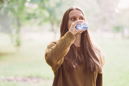 秋天或冬天，年轻漂亮的女孩在公园的街道上用塑料瓶喝水。