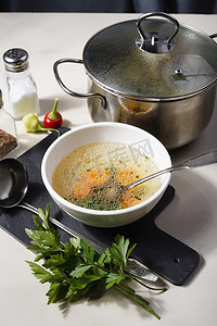 一个碗和一个锅，里面装着新鲜的自制鸡汤、香料和欧芹。