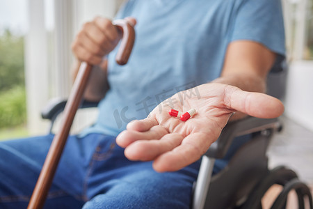 在疗养院里，正在康复中的生病老人拿着他的药物，坐在轮椅上用手杖。