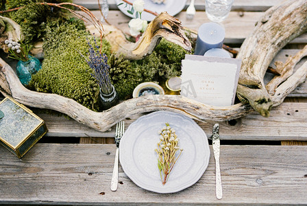 干花花束摄影照片_桌子上婚礼请柬附近的盘子上有一束干花。