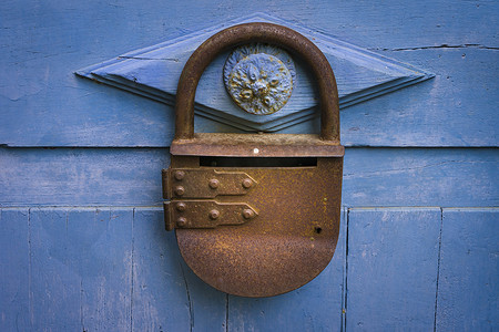 一扇蓝色油漆木门的特写照片，上面有一把古董生锈的金属挂锁。