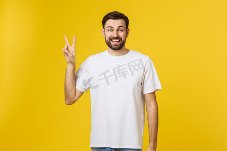 年轻英俊的男子穿着条纹 T 恤，在孤立的黄色背景上微笑着看着镜头，手指在做胜利的手势。