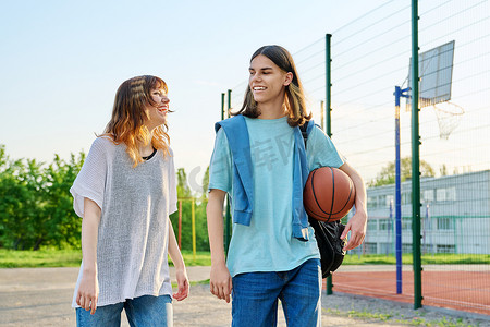 行走男摄影照片_篮球场附近带球在户外行走的年轻男女学生
