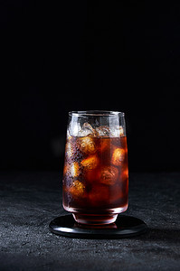可乐摄影照片_深色背景高玻璃杯中的冰可乐或冷咖啡。