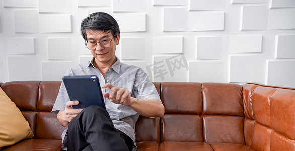 亚洲老人在客厅的沙发上玩平板电脑和视频通话