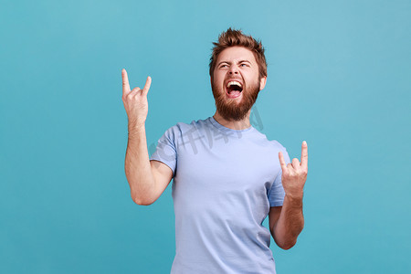 身穿蓝色 T 恤的男子展示摇滚手势重金属标志，在派对上享受最喜欢的音乐。